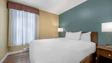 A hotel room with a large bed, bedside lamps, a window with curtains, and a wooden floor.