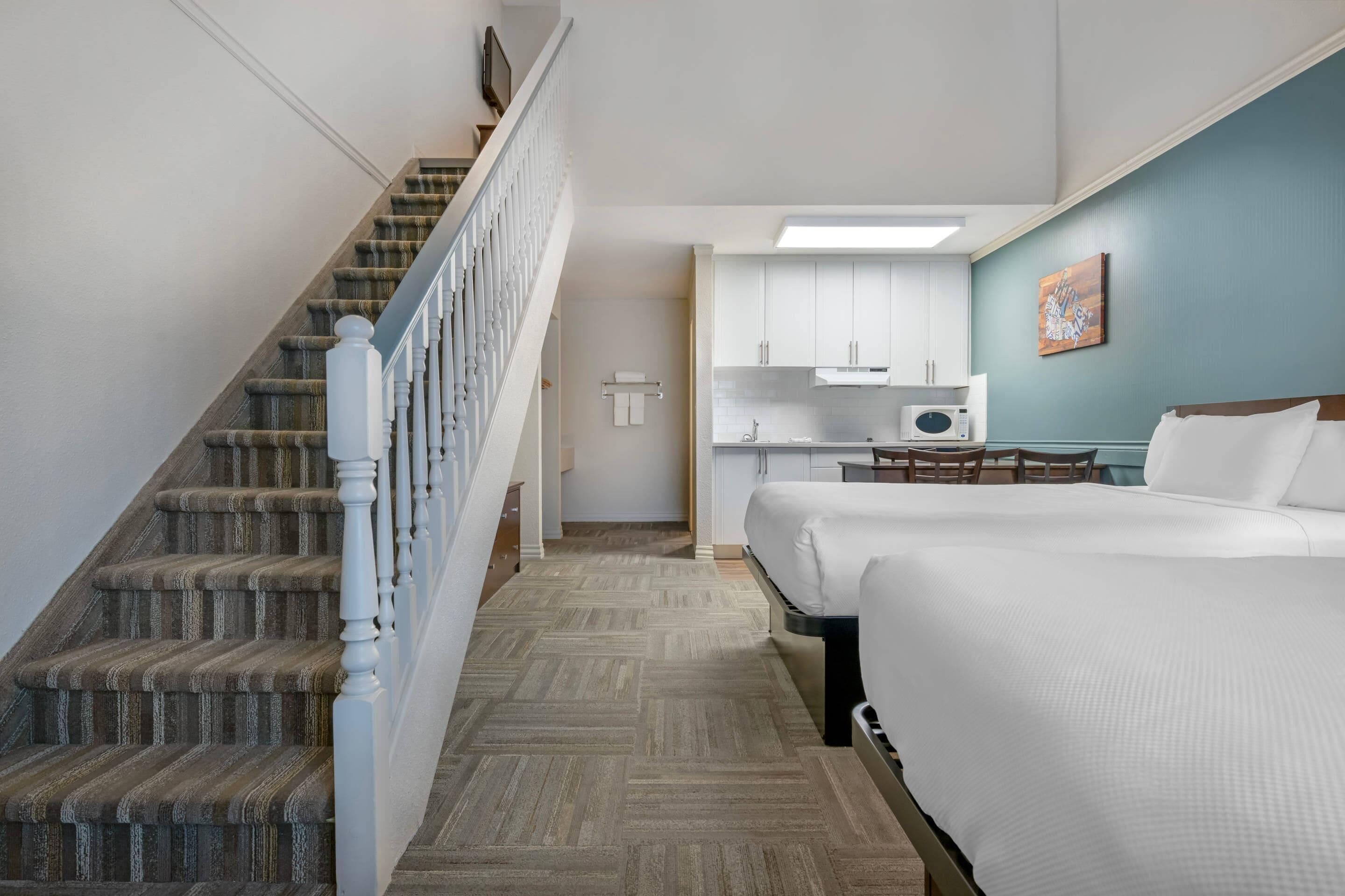 A hotel room with a staircase, a bed, a kitchenette, and a door leading to another room.