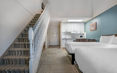 A hotel room with a staircase, a bed, a kitchenette, and a door leading to another room.