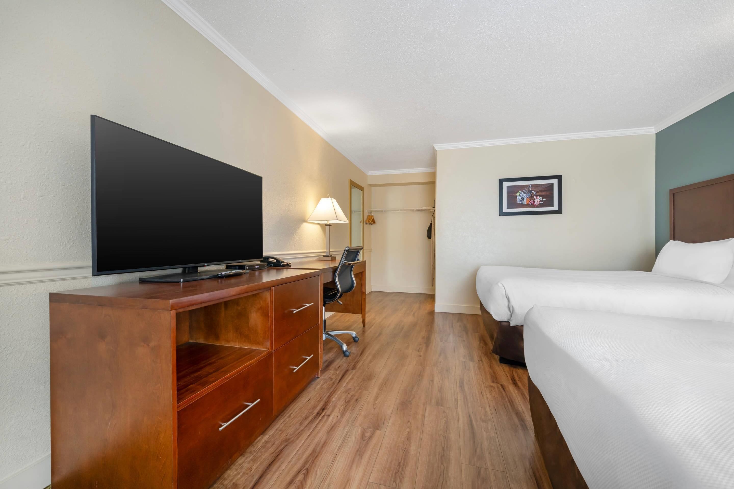 A hotel room with a bed, a TV on a wooden cabinet, a desk with a chair, and a coat rack.