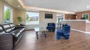 A modern hotel lobby with a leather sofa, blue armchairs, a reception desk, and a large window offering a view of the outside.