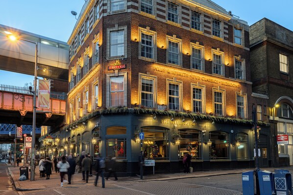 A historic building with multiple stories, featuring a ground-floor pub with outdoor seating and a sign indicating it is a public house. - The Wellington Hotel (London)