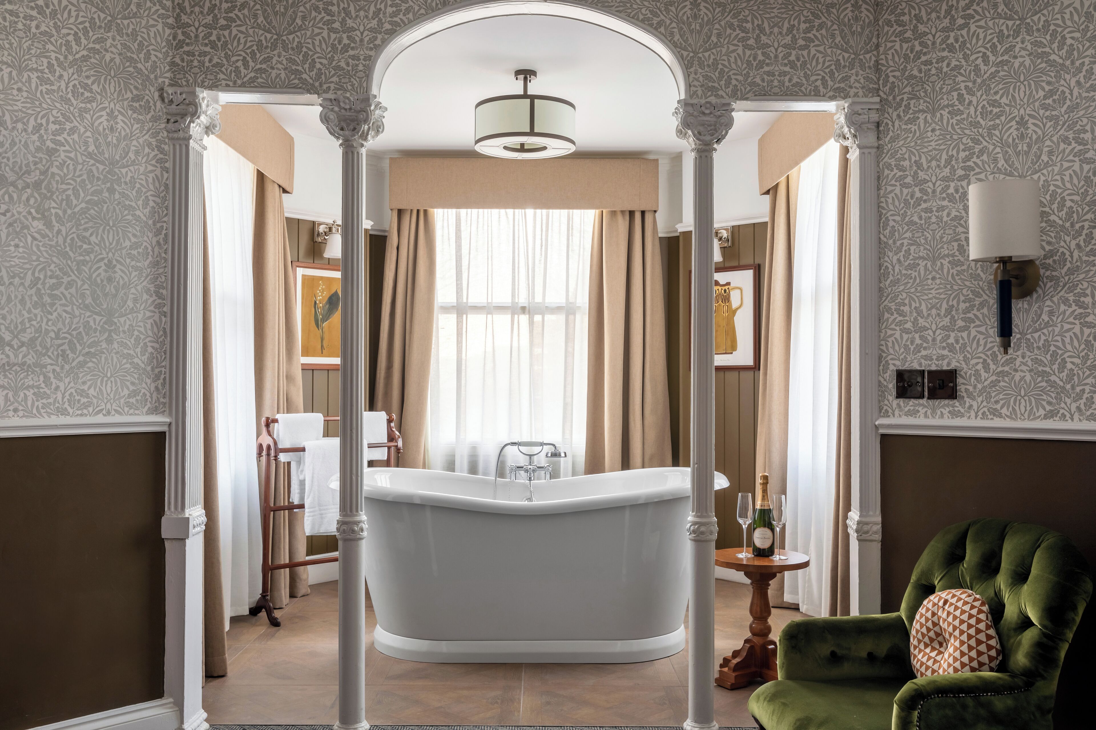 A classic bathroom with a freestanding bathtub, a green armchair, and a chandelier.