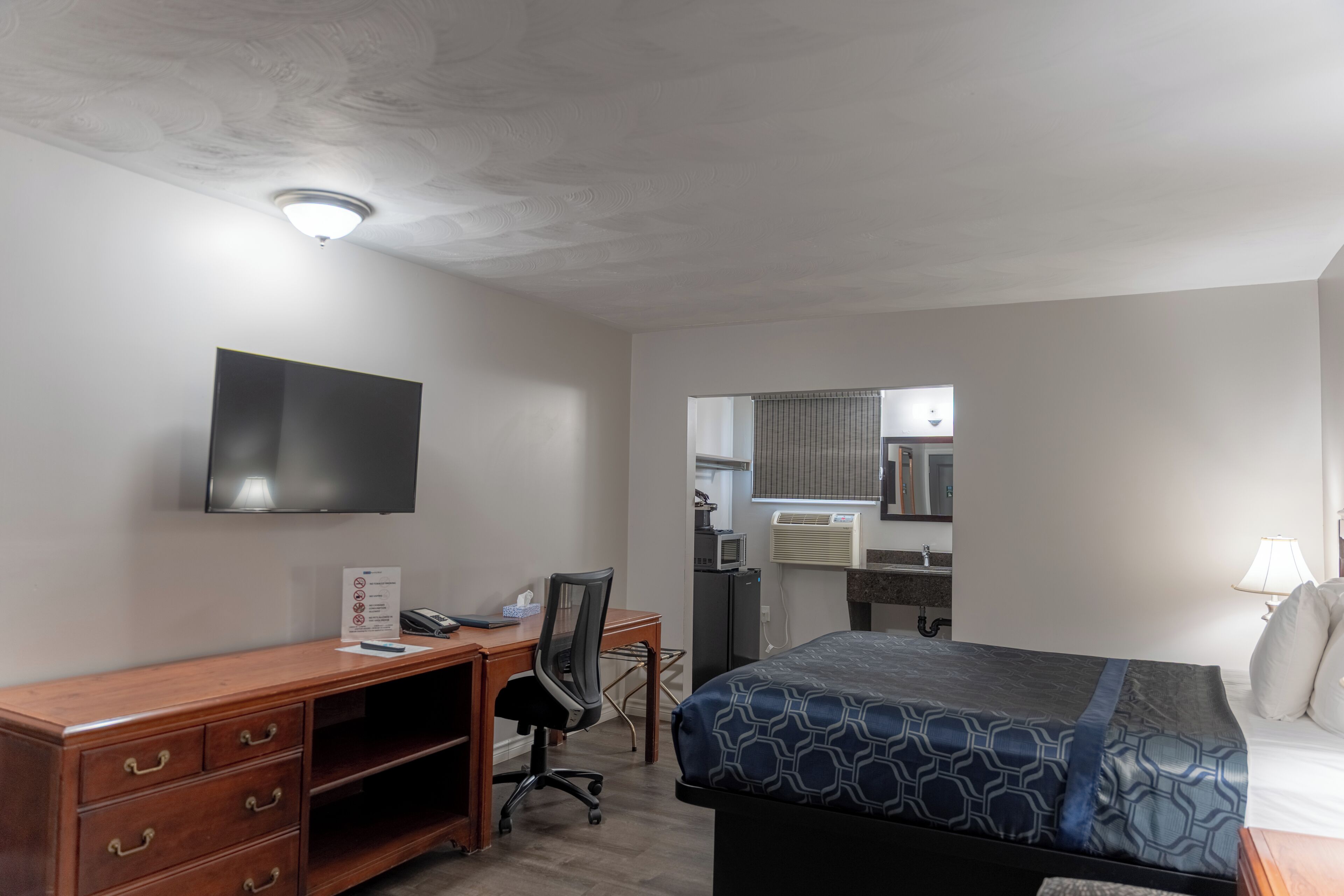A hotel room with a bed, desk, chair, television, and a bathroom visible through an open door.