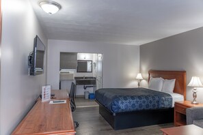 A hotel room with a bed, bedside table, lamp, desk, chair, and a bathroom with a sink and mirror. - Aquarius Motel (Tay Valley)