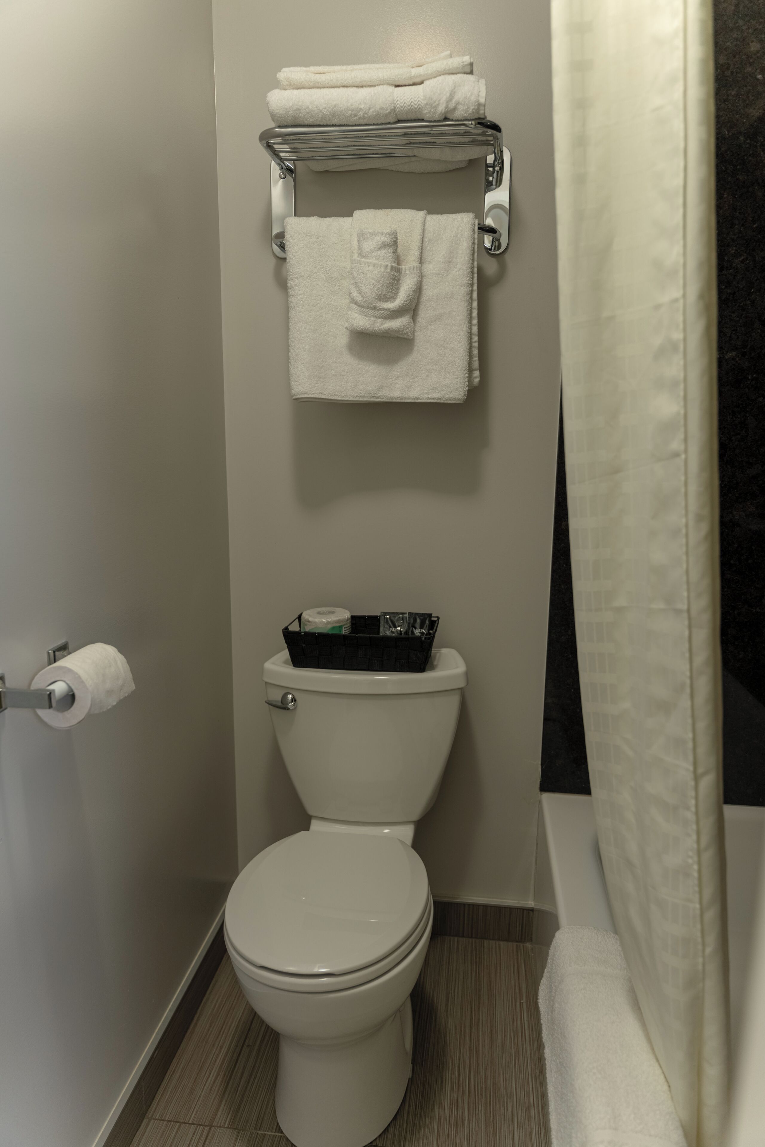 Un baño con inodoro, toallero con toallas dobladas, porta papel higiénico y cortina de ducha.
