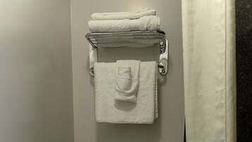 Un baño con inodoro, toallero con toallas dobladas, porta papel higiénico y cortina de ducha.