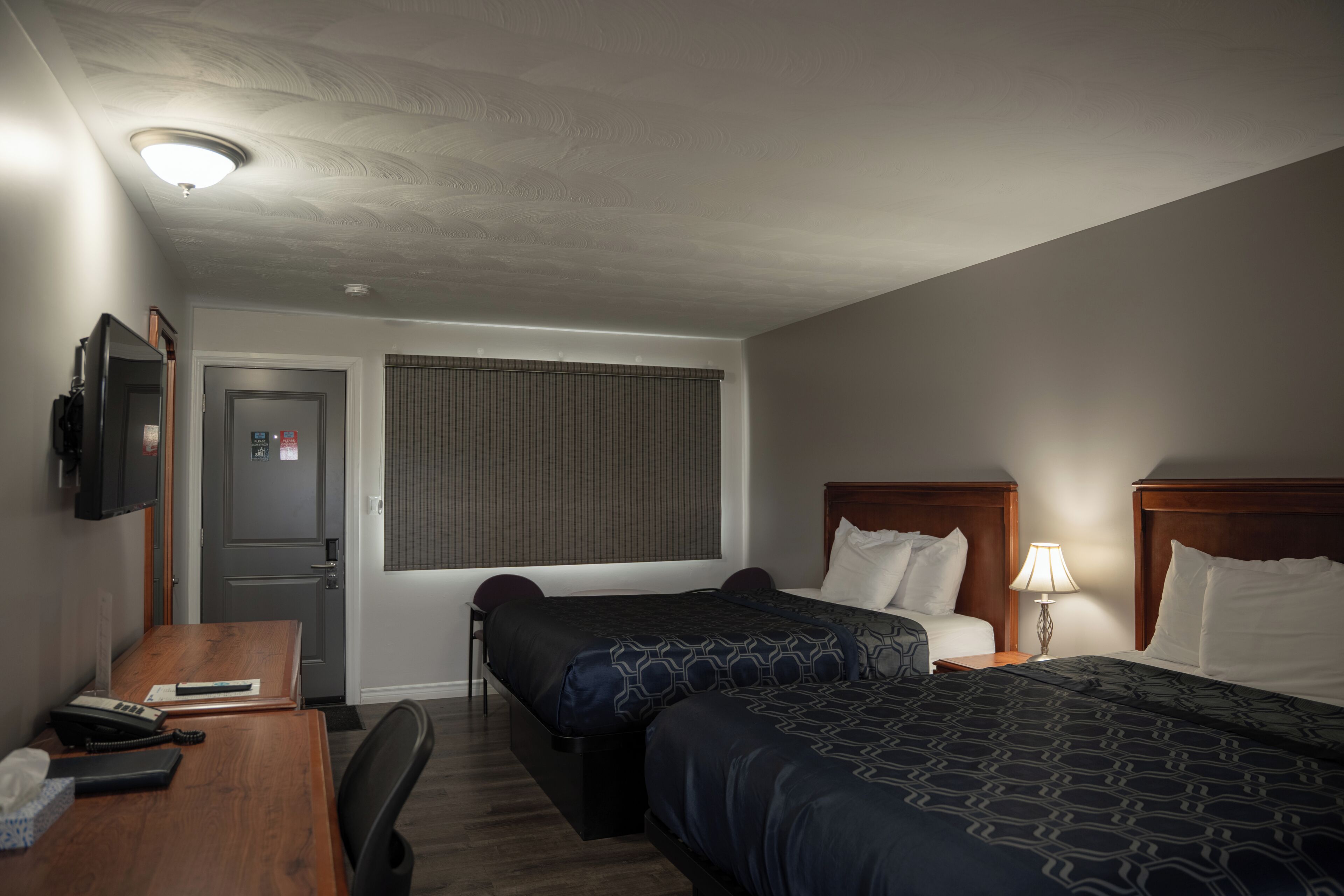A hotel room with two beds, a desk, a television, and a window with blinds.