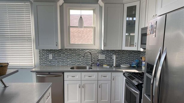 A modern kitchen with white cabinets, a stainless steel refrigerator, and a tiled backsplash.