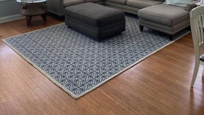 A living room with a sectional sofa, ottoman, patterned rug, and a small round table.