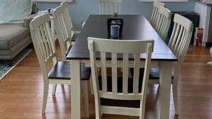 A dining area with a table and chairs, a sofa, and two windows with blinds.