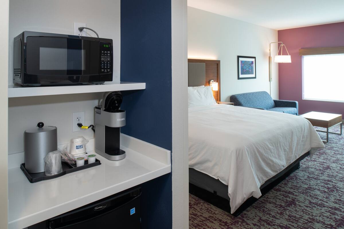 A hotel room with a microwave, coffee maker, and a bed with white bedding.
