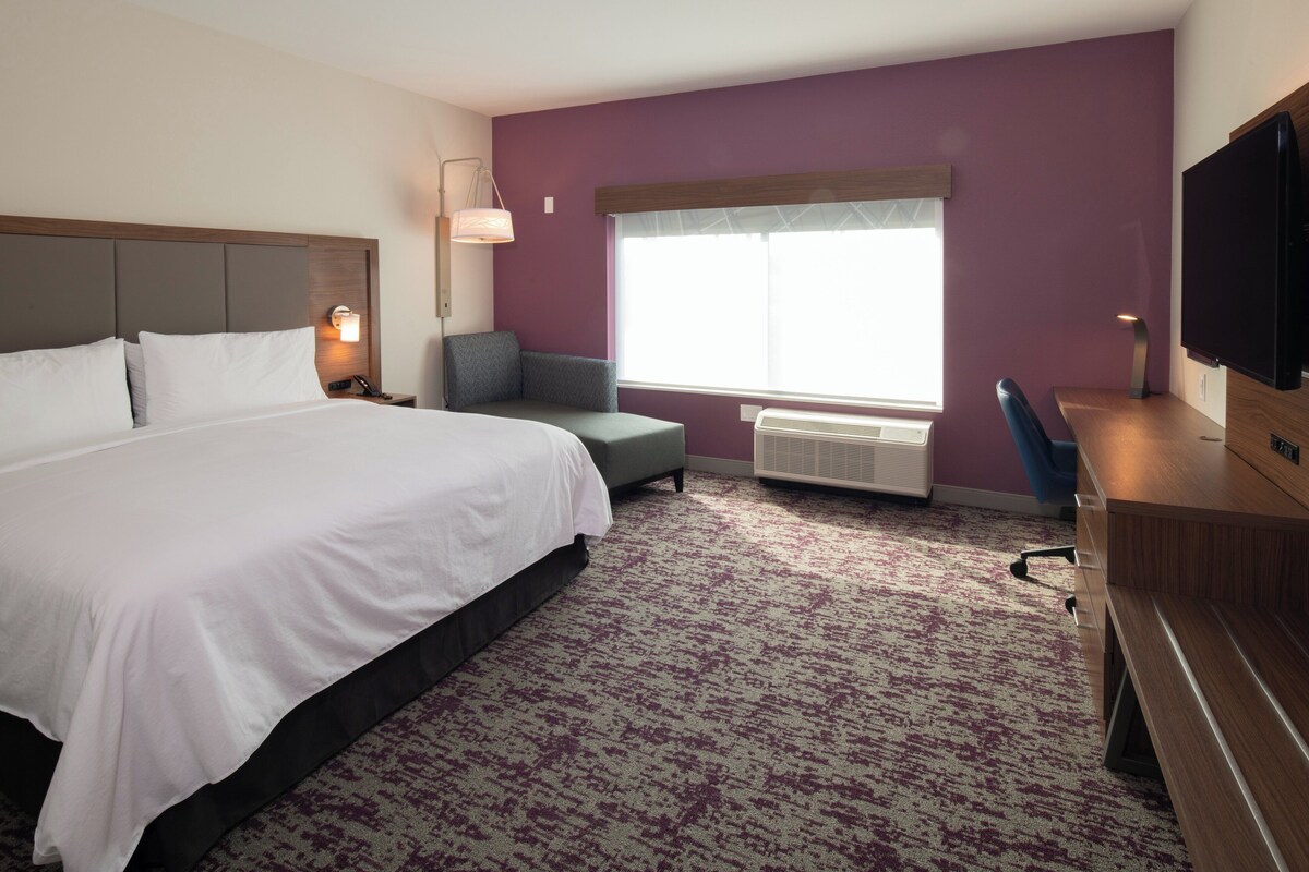 Een hotelkamer met een groot bed, een bureau, een stoel, een televisie en een raam met zonwering.
