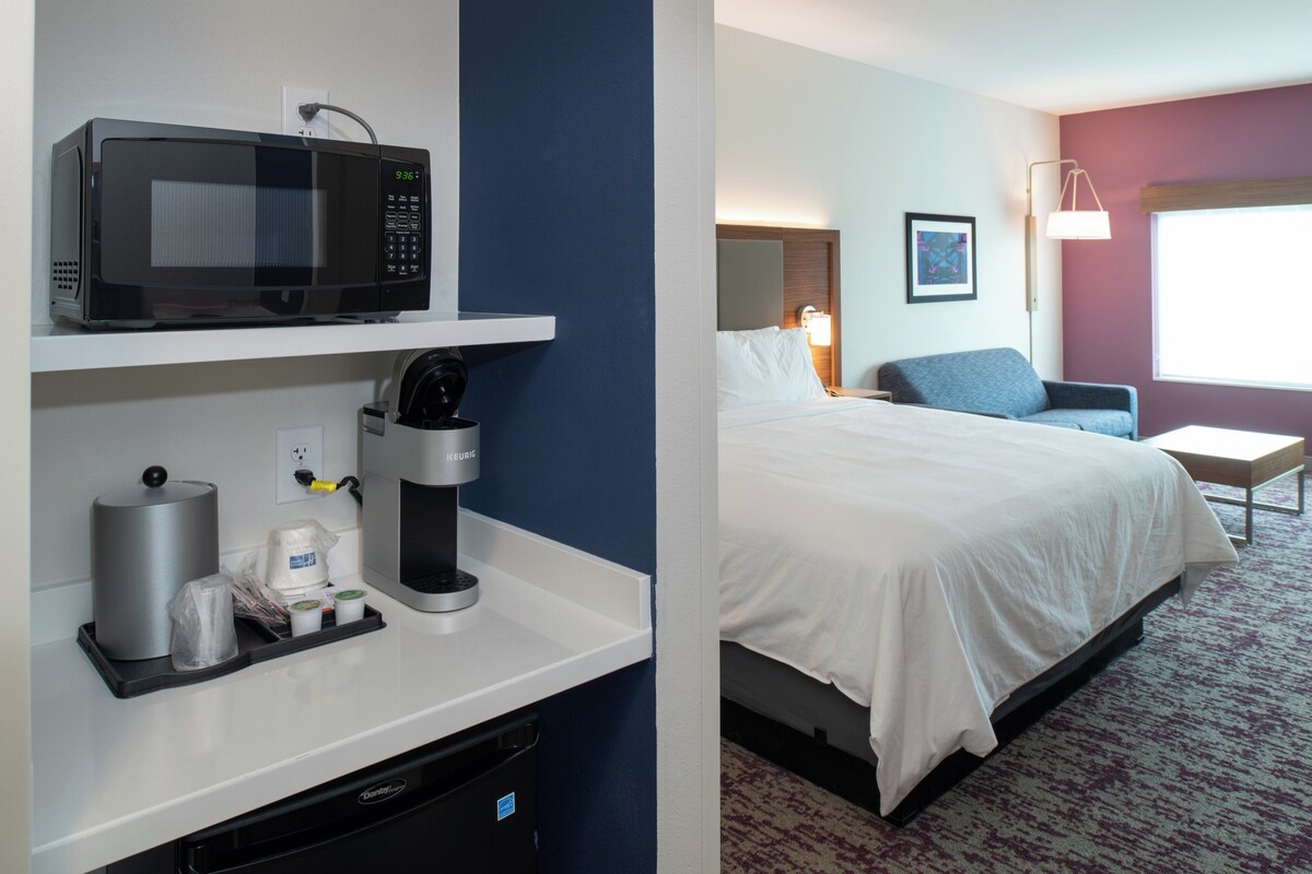 Een hotelkamer met een magnetron, koffiezetapparaat en een bed met wit beddengoed.
