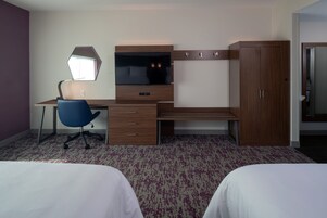 A hotel room with a bed, a desk with a chair, a TV, and a wardrobe.