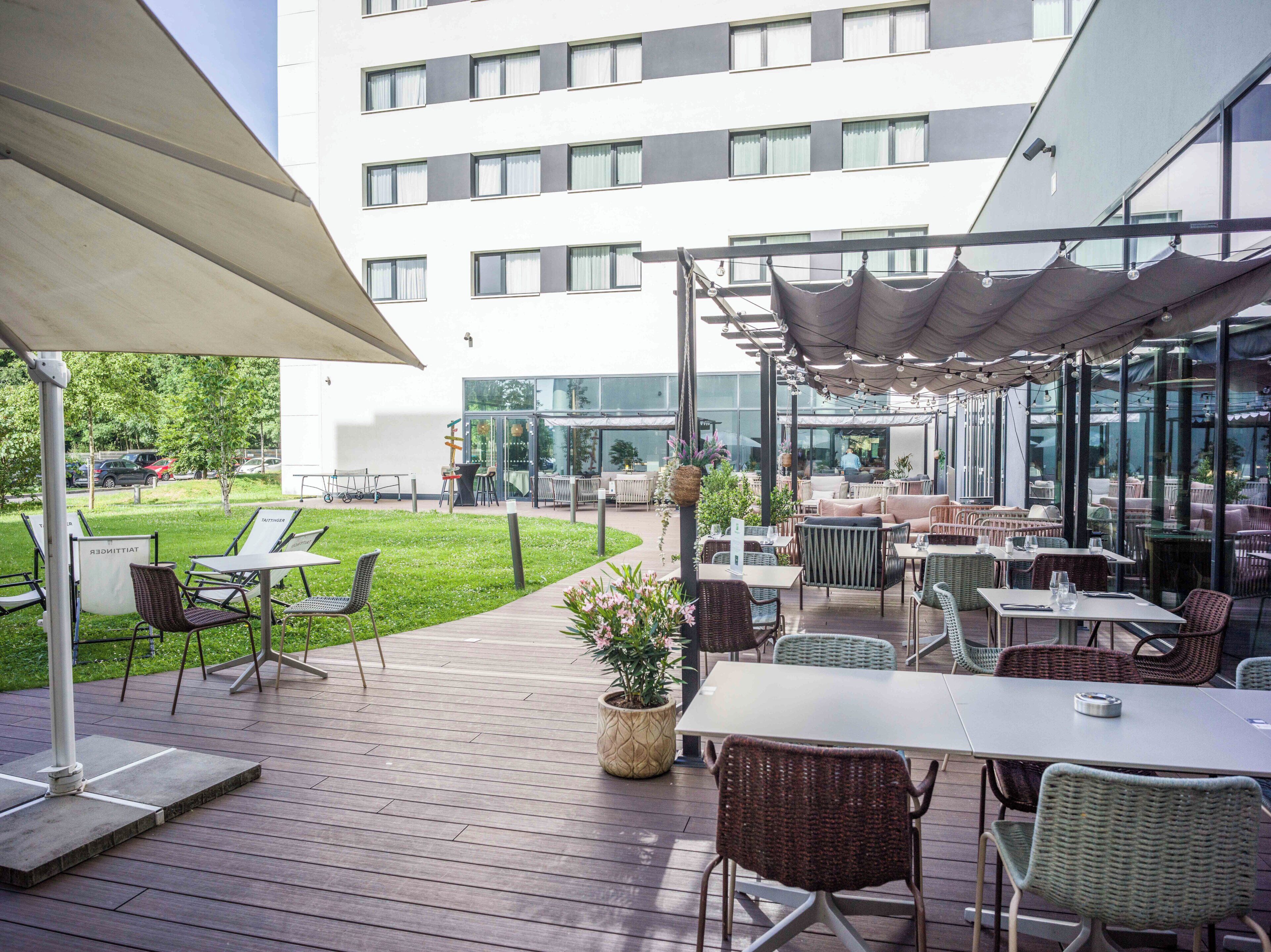 An outdoor patio area with tables and chairs, a grassy lawn, and a building with multiple windows in the background.
