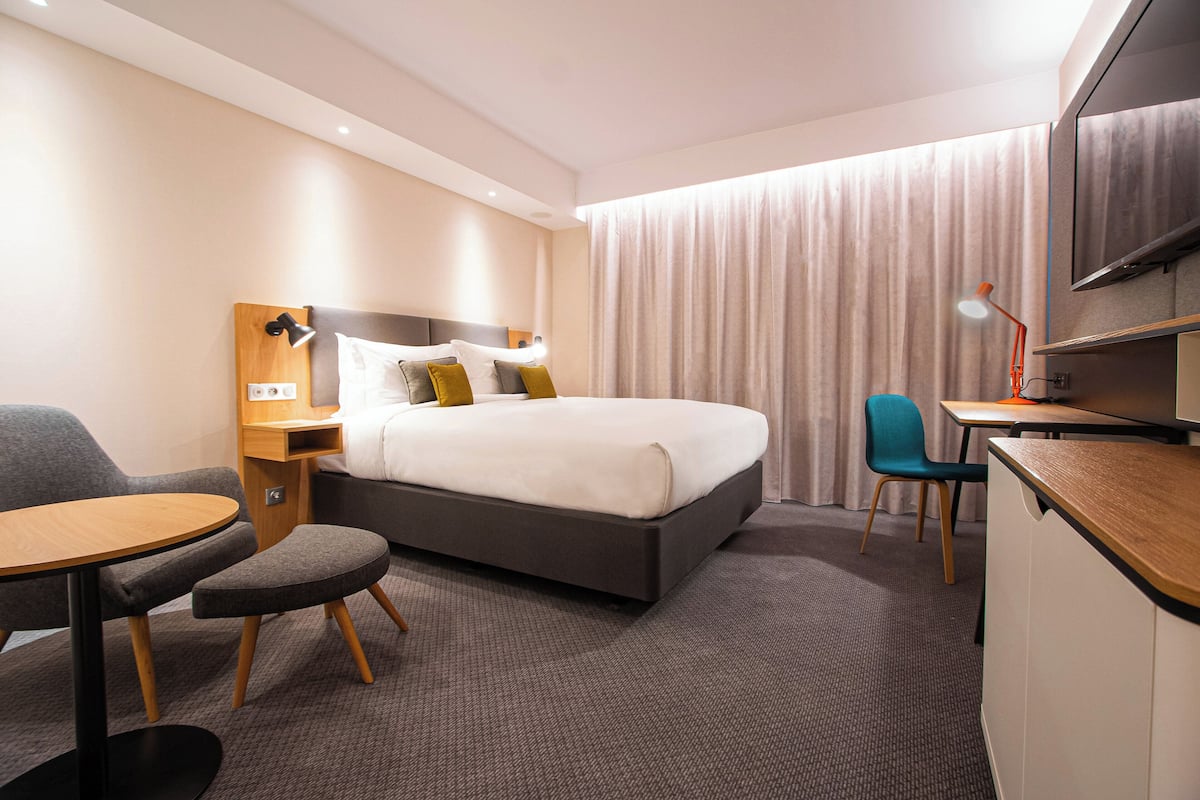 A hotel room with a bed, a desk, a chair, and a television.