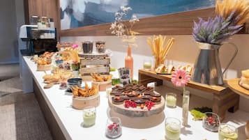 A buffet table with various food items and drinks, including pastries, desserts, and beverages, arranged on a white table with a modern design.