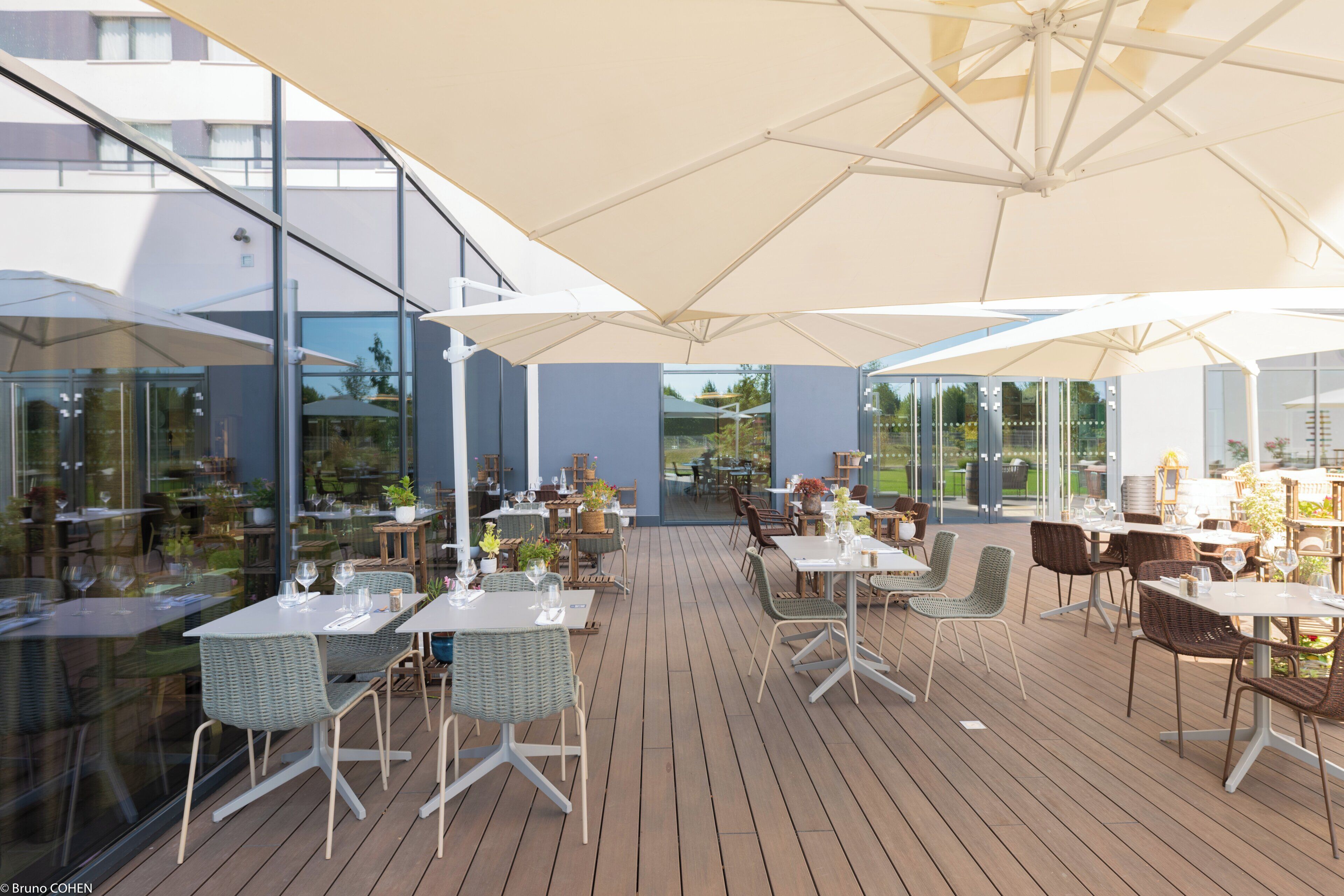 An outdoor dining area with tables and chairs, large umbrellas, and glass walls.