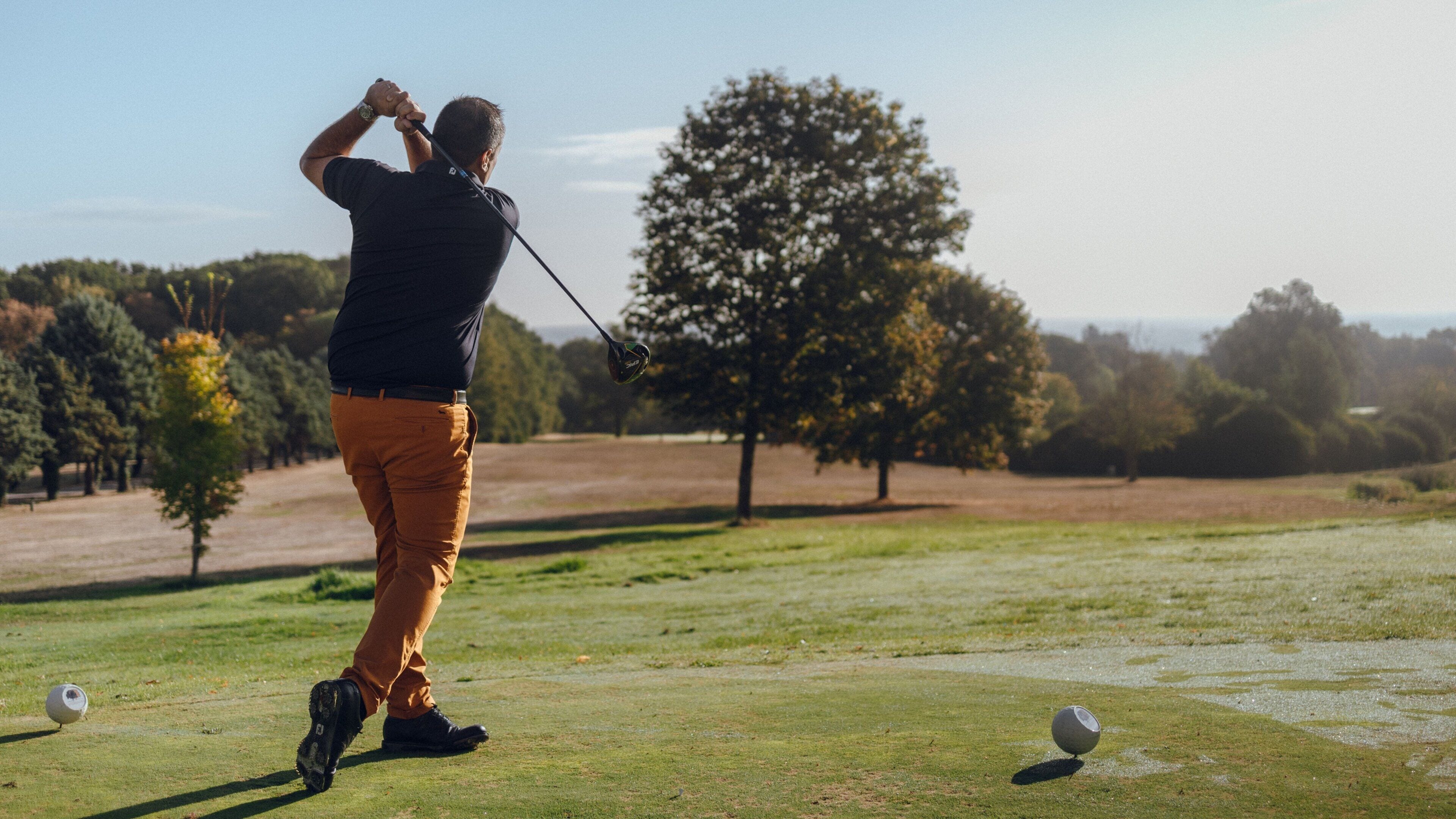 A person playing golf on a course with trees and a clear sky.