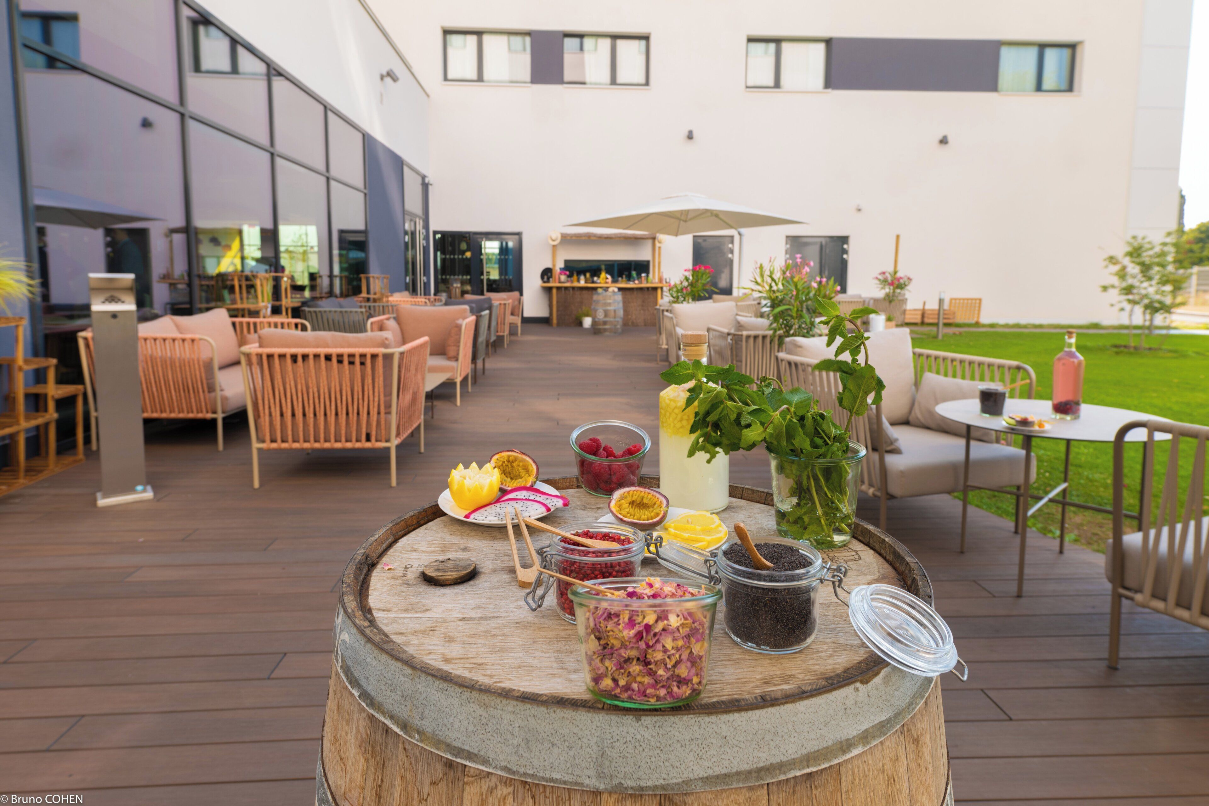 Un espace extérieur aménagé en terrasse, avec des meubles en bois, un bar et divers produits alimentaires et boissons présentés sur un tonneau.