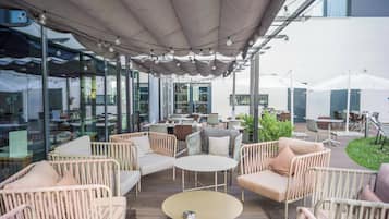 Un espace extérieur aménagé avec des meubles en osier, des tables rondes et un coin abrité décoré de guirlandes lumineuses.