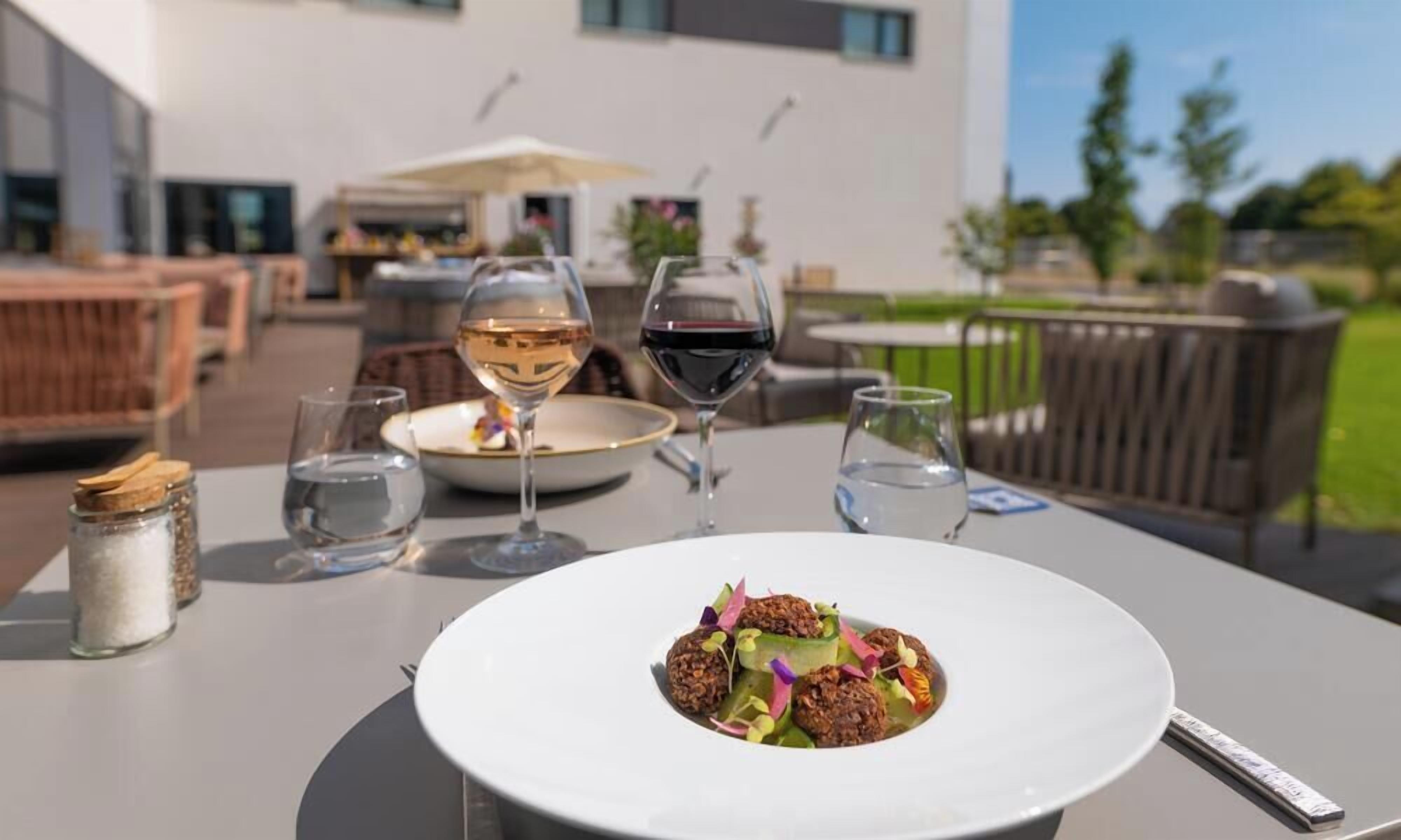 An outdoor dining area with a white table, a plate of food, and two wine glasses.