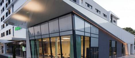 A modern hotel with a glass facade, a flat roof, and a visible conference room.
