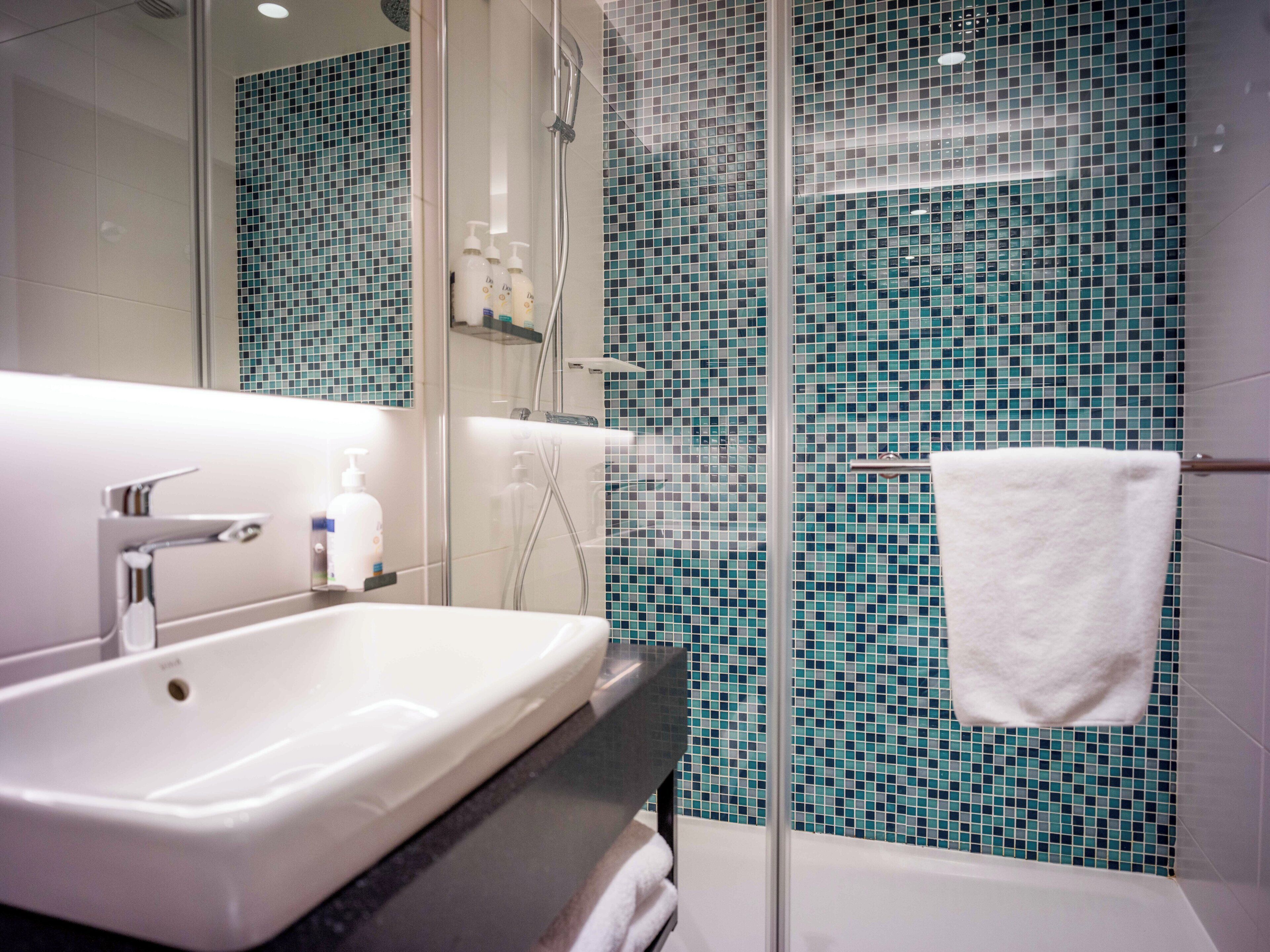 A bathroom with a white sink, a glass shower enclosure, and a tiled wall.