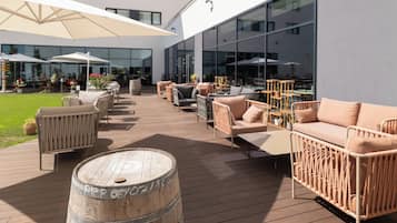 An outdoor patio area with wicker furniture, a wooden barrel, and umbrellas.
