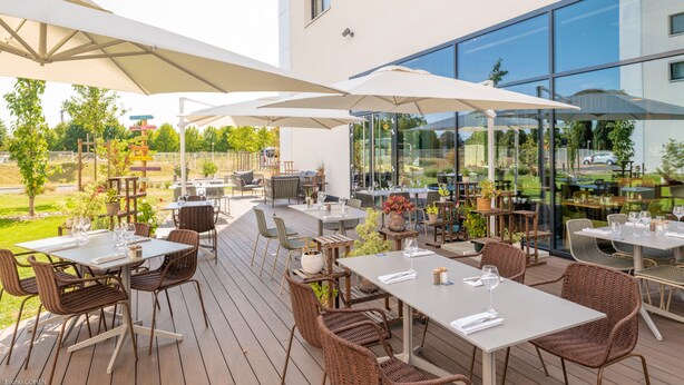 An outdoor dining area with tables and chairs, umbrellas, and potted plants. - Holiday Inn Paris CDG Airport by IHG (Roissy-en-France)