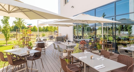 An outdoor dining area with tables and chairs, umbrellas, and potted plants.. Holiday Inn Paris CDG Airport by IHG