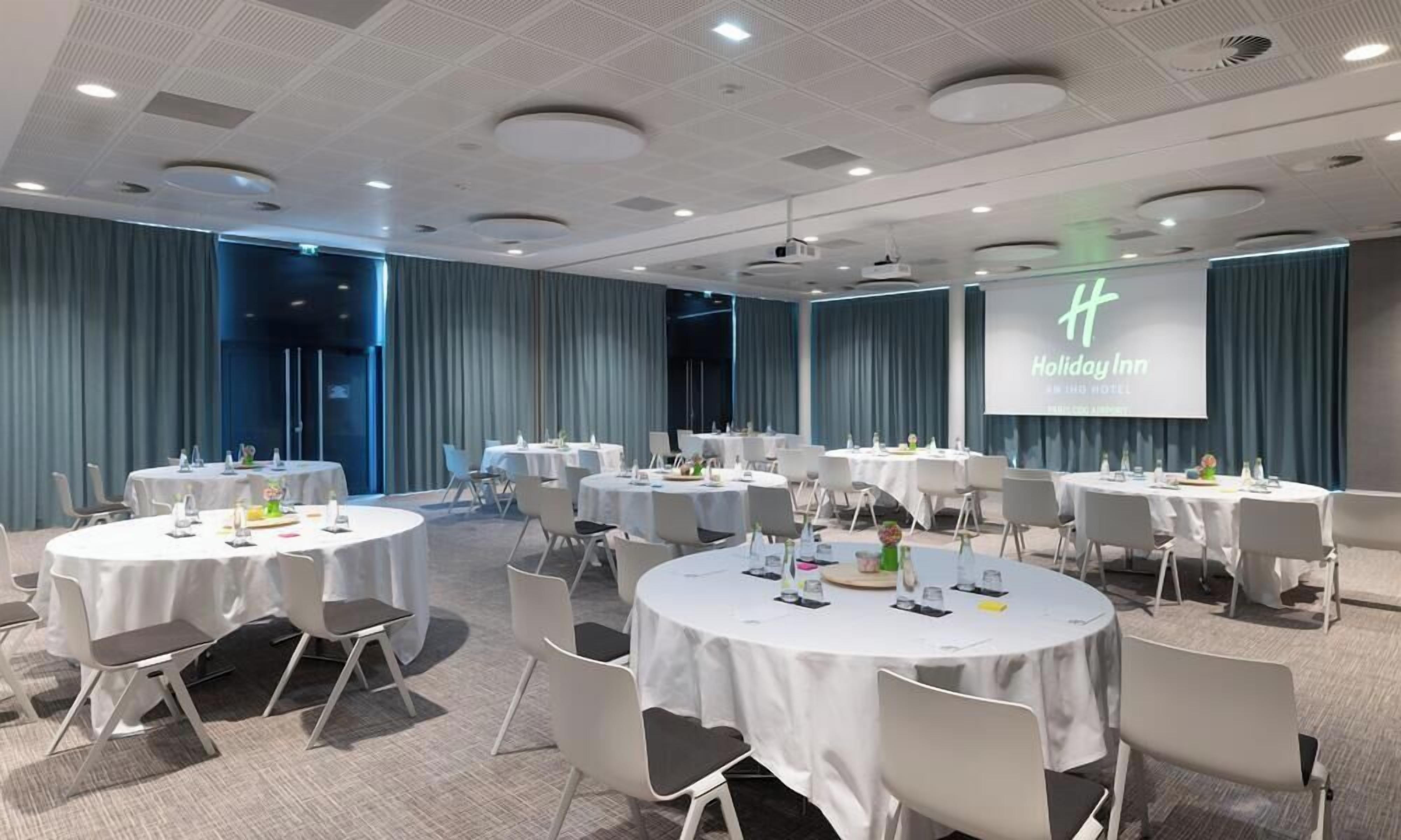 A conference room with multiple round tables, each set with chairs and tableware, in a modern hotel setting.