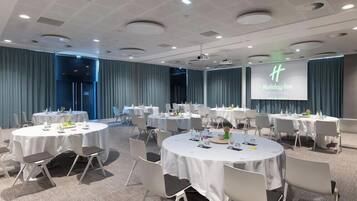 A conference room with multiple round tables, each set with chairs and tableware, in a modern hotel setting.