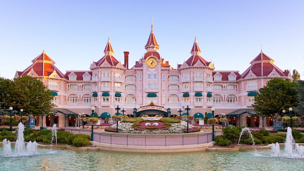 A large, pink, multi-story building with a central clock tower, surrounded by a fountain and greenery. - Holiday Inn Paris CDG Airport by IHG (Roissy-en-France)