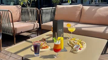 Una mesa con bebidas y un plato de comida, un letrero de bar y asientos al aire libre.