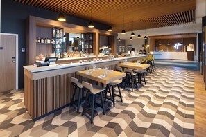 Un espace bar moderne doté d’un long comptoir, de nombreux sièges et d’un sol à motifs.