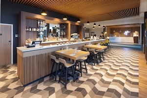 Uma área de bar moderna com um balcão comprido, diversas opções de assento e piso estampado.