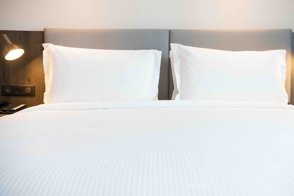 A neatly made bed with white linens, two bedside lamps, and a telephone on the left side.
