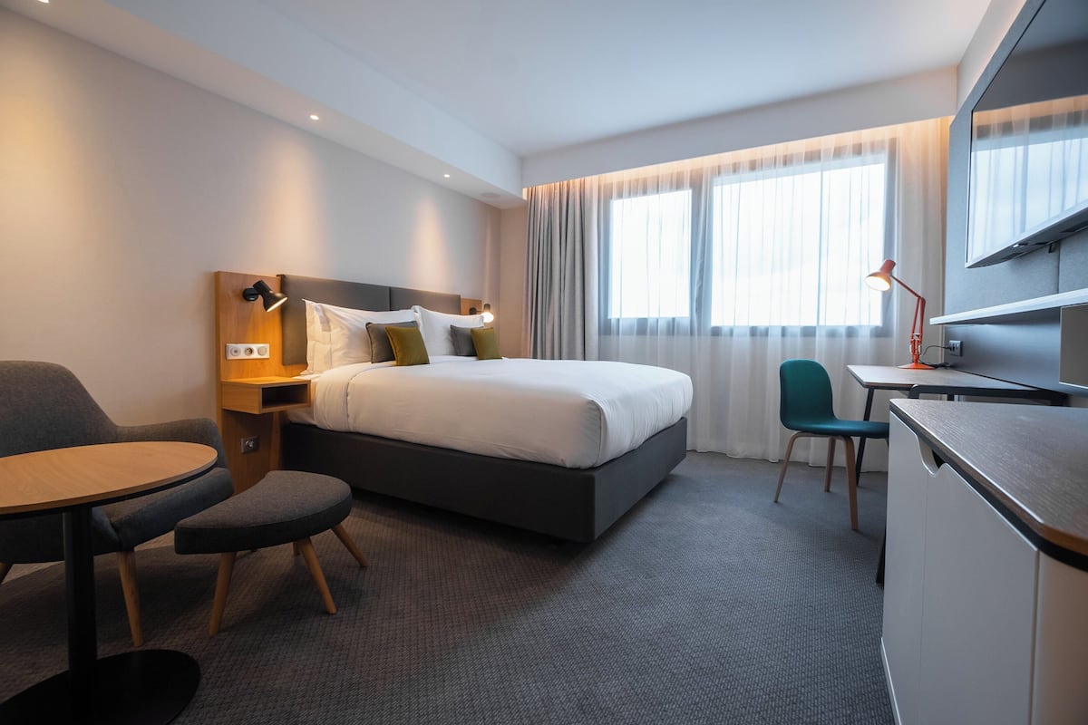 A modern hotel room with a large bed, a desk, a chair, and a TV.