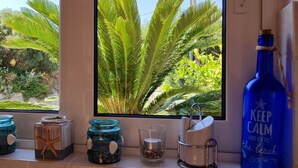 Una finestra con vista su vegetazione rigogliosa e una bottiglia blu con testo.