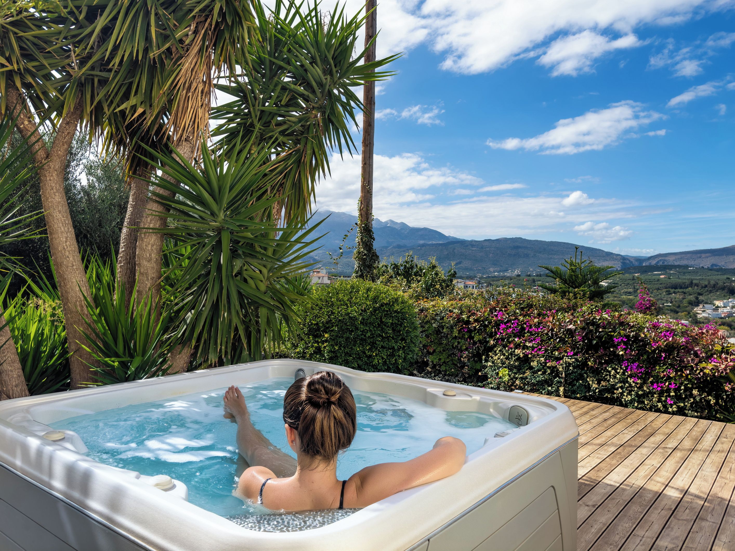 A person relaxing in a hot tub with a scenic view of mountains and greenery.