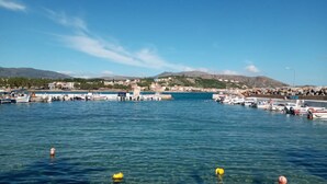 Una marina costiera con imbarcazioni ormeggiate, acqua limpida e montagne sullo sfondo.