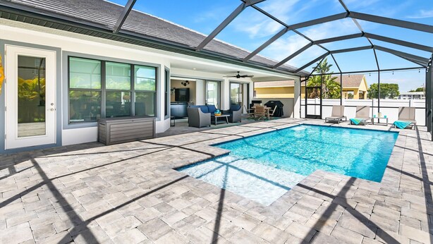 A covered outdoor swimming pool with a patio area, seating, and a ceiling fan.