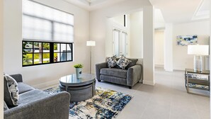 A modern living room with a grey sofa, a round coffee table, and a large window with blinds.