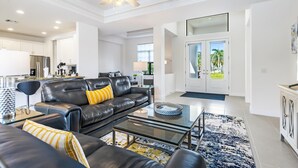 A modern living room with a black leather sofa, a glass coffee table, and a blue patterned rug.
