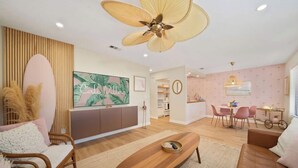 Een moderne woonkamer met een grote flatscreen-tv, een houten salontafel, een bank en een eethoek met roze stoelen.