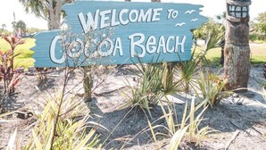 Welkomstbord voor Cocoa Beach, met een tropische achtergrond.