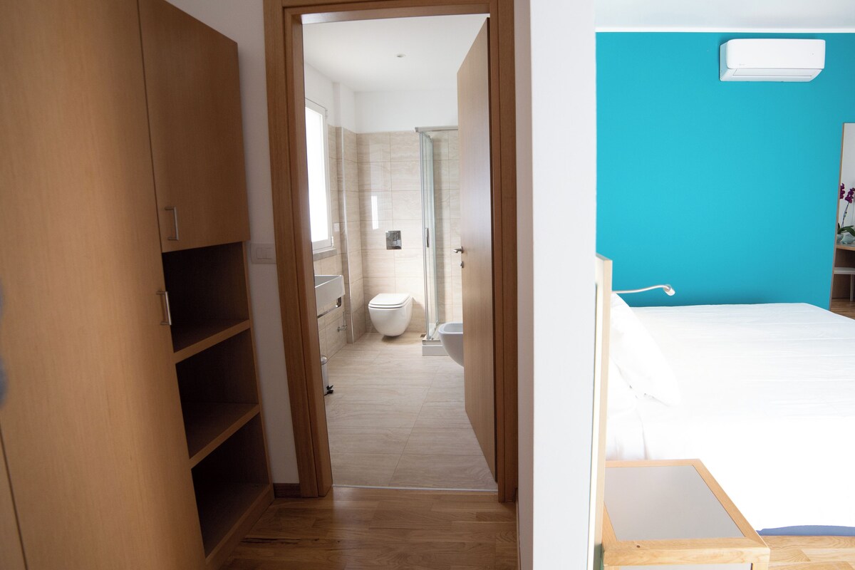 A bedroom with a bed, a wooden wardrobe, and a bathroom with a toilet and shower.
