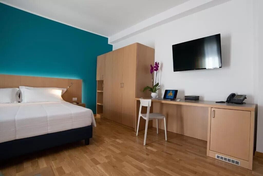 A hotel room with a bed, a desk, a chair, a television, and a wardrobe.